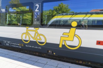 Train with bicycle and wheelchair symbols on a sunny platform surface, battery Electric train with