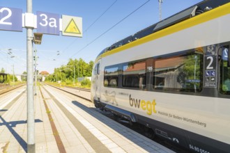 Modern train at a sunny railway station with blue sky and trees in the background, battery Electric