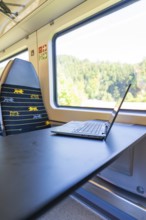 Laptop on a folding table in front of a window with a view in a vehicle, battery Electric train