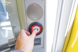Hand operates a red illuminated stop button on a door in the vehicle, battery Electric train with