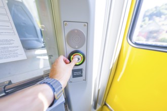 Hand presses stop button on a yellow door in the interior, battery Electric train with green