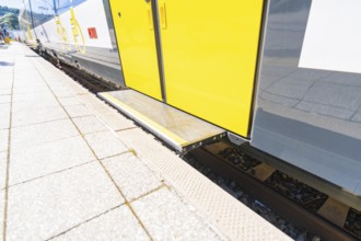 Close-up of the boarding area of a yellow and white train on the track, battery Electric train with
