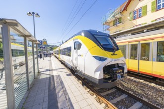 Yellow and white train at a stop, busy railway station under a clear sky, battery Electric train