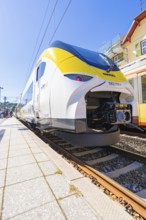 Yellow and white train on the tracks, slight angle of view from below at the station, battery