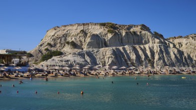 Lively beach against a rocky backdrop with bathing facilities and numerous parasols, Limanaki