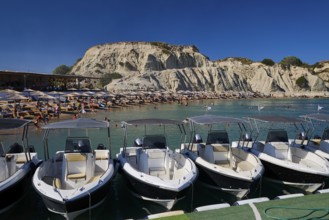 Boats in front of a rocky beach section with holiday atmosphere, many bathers and sunshades