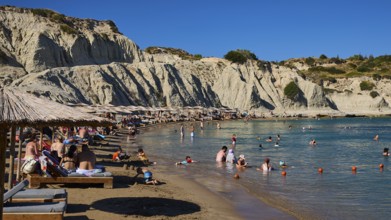 Pleasant scenery on the beach with beach loungers, bathers and magnificent rocky backdrop, Limanaki