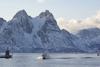 A motorboat sailing through the cool sea in front of snow-covered mountains in winter, Myre,