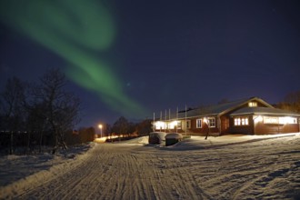 A snowy path leads to a house under the Northern Lights and a clear night sky, Sortland campsite,
