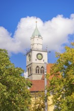 Church tower with clock rises above trees under a blue sky with clouds, Lake Constance, Germany