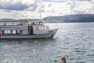 Small ship sailing on a lake with urban shore in the background, Lake Constance, Germany
