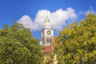 Church tower with red roof and clock above trees under a blue sky, Lake Constance, Germany
