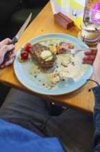 Person eating a steak with tomatoes and garnish on a blue plate, Lake Constance, Germany