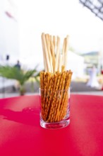 A glass container with breadsticks stands on a red table in an outdoor event area, Lake Constance,