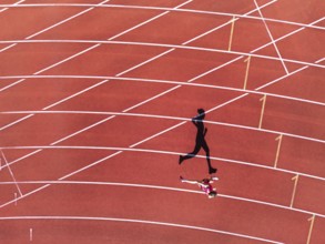 Aerial view of a female individual (runner) on a red athletics track (tartan track) with shadow as