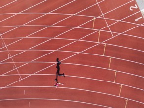 Aerial view of a female individual (runner) on a red athletics track (tartan track) with shadow as