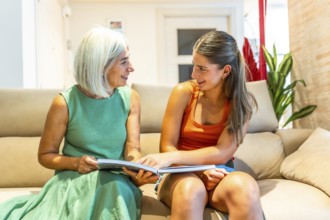 Smiling senior woman and young woman reading a book together on a comfortable sofa in the living