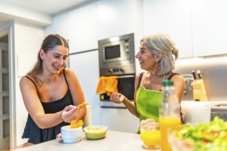 Two women, one older and one younger, enjoying healthy snacks together in a modern kitchen,