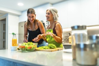Older and younger women enjoying time in a modern kitchen, preparing a fresh salad. Laughter and