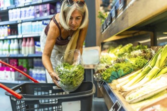 Senior woman picking fresh lettuce in the produce section of a grocery store, putting vegetables in