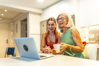 Happy senior woman and her daughter are drinking coffee and having a video call on a laptop in a