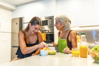 Elderly woman and young woman sharing a joyful moment in a modern kitchen, preparing food and