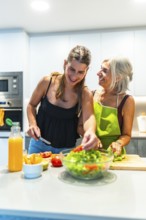 Elderly woman and young adult preparing a fresh salad together, showcasing family connection and