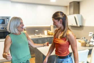 Senior mother and adult daughter having fun dancing together in a bright modern kitchen, enjoying