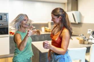 Happy mother and daughter are dancing together in their modern kitchen, enjoying a carefree moment