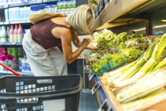 Woman selecting fresh vegetables in a grocery store, placing items in a basket, emphasizing healthy