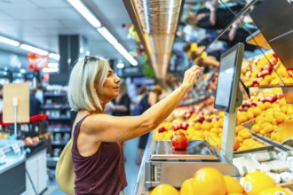 Senior woman using a digital weight scale to weigh fresh fruits at the supermarket, selecting her