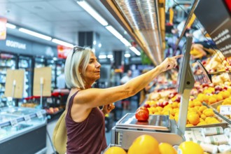 Mature woman shopping for fresh produce in a grocery store, using a digital scale to weigh fruits