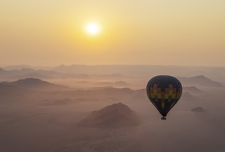 The hot-air balloon above an arid plain and isolated mountain ridges at the edge of the Namib