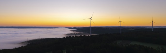 Row of wind turbines along the horizon at sunrise with fog in the distance, near Schorndorf,