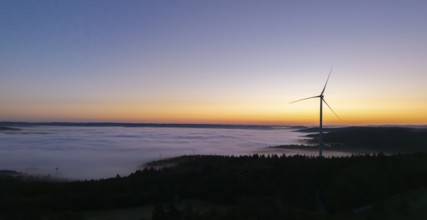 Single wind turbine above a sea of fog against a colourful morning sky, near Schorndorf, Remstal,