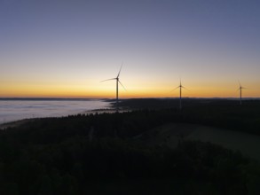 Three wind turbines in front of an orange and blue sky at sunrise with fog, near Schorndorf,