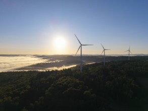 Three wind turbines stand in the early morning light above a misty valley, near Schorndorf,
