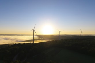 Three wind turbines in the soft morning light over a misty forest landscape, near Schorndorf,
