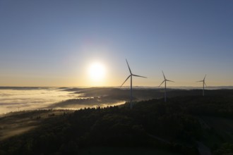 Wind turbines rise into the sky above a misty forest at sunrise, near Schorndorf, Rems-Murr-Kreis,