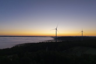 Two wind turbines in front of a colourful sunrise sky with fog over the landscape, near Schorndorf,