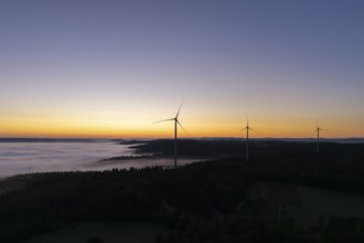 Wind turbines in front of a bright blue and orange sky at sunrise with fog over the landscape, near