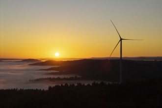 A wind turbine stands over the hills in front of sunrise, near Schorndorf, Rems-Murr district,