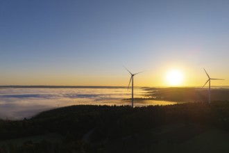 Two wind turbines rise above a fog-covered landscape in the morning light, near Schorndorf,