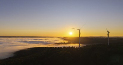 Wind turbines stand in the morning mist under a clear sunrise sky, near Schorndorf, Rems-Murr