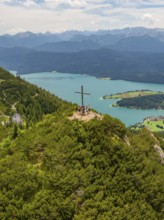 Group on a mountain with summit cross, overlooking a wide lake landscape, Herzogstand summit,