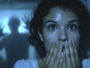 A woman gripped by fear, behind her an eerie silhouette of a shadow, symbolic image for anxiety