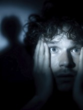 An anxious man with wide open eyes staring into the darkness, shadow in the background, symbolic