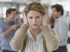 A young woman with her hands to her ears, annoyed by an argument or noise in the background,