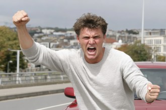 A man shouts angrily with clenched fists on a road, symbolic image for aggressive behaviour in road