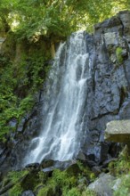 Vaucoux waterfall cascades gracefully over dark rocks, surrounded by lush greenery, Auvergne